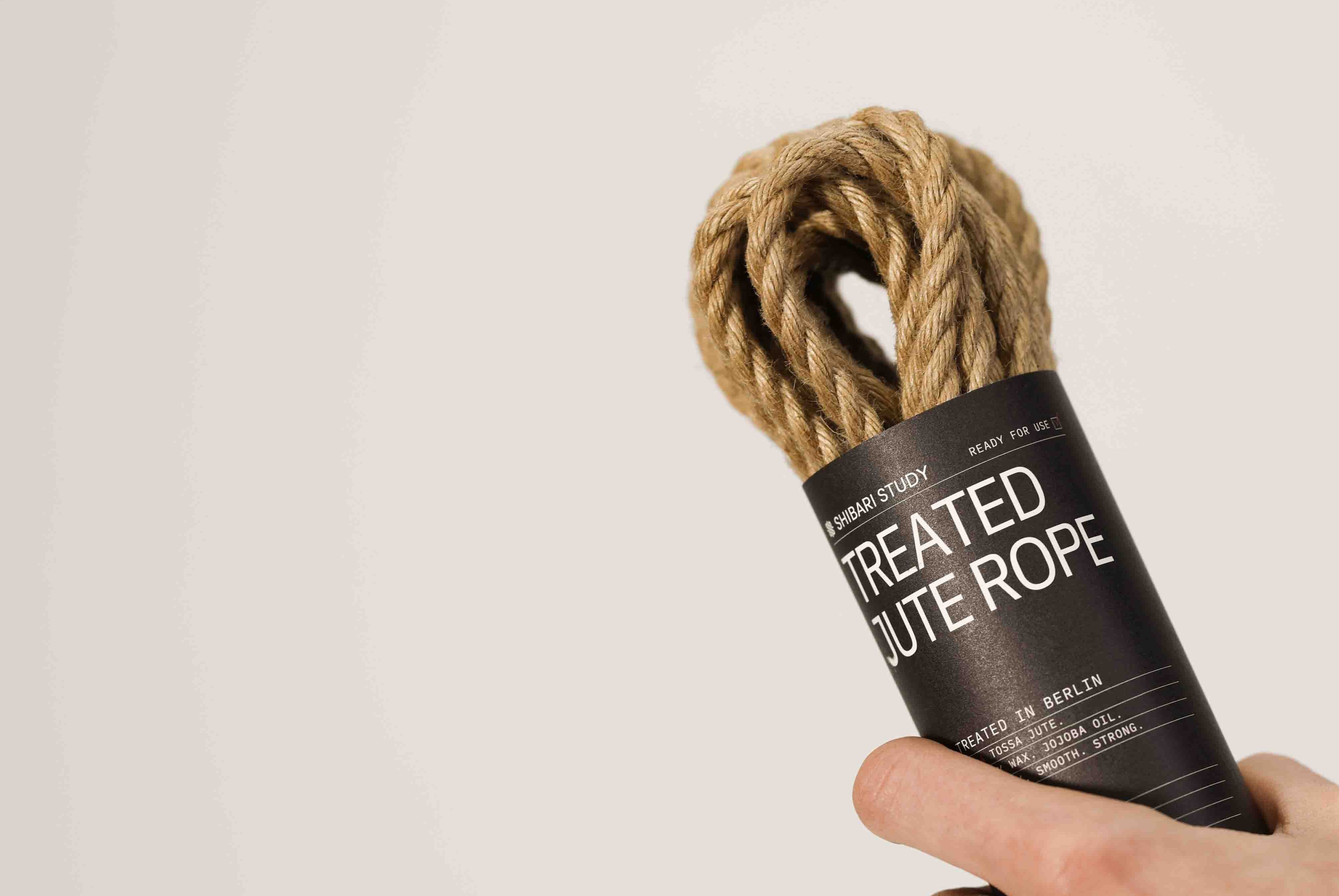 Hand holding treated jute rope with a label on a plain background